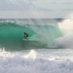 man riding surfboard under sea wave during daytime